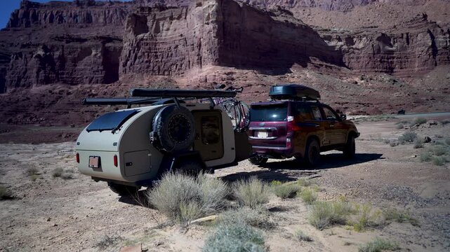Adventurers navigate rocky paths in Glen Canyon, Utah, with an SUV towing a teardrop camper trailer, embracing the wild outdoors.