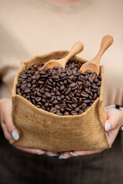Close up of a person holding a rustic burlap bag filled with roasted coffee beans and wooden scoops.
