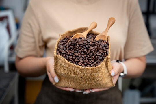 Hands holding a small jute sack containing freshly roasted coffee beans and wooden spoons.