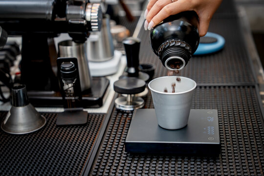 Barista pours coffee beans into a metal dosing cup on a digital scale.