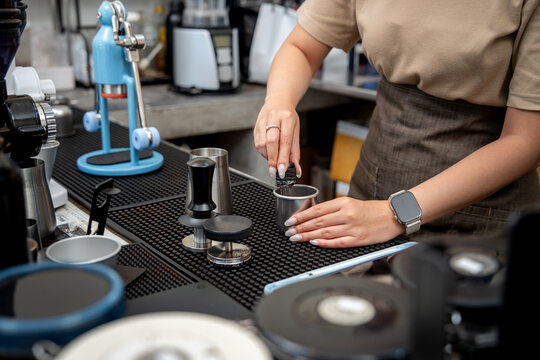 Barista using coffee distribution needles in a metal dosing cup before espresso preparation.