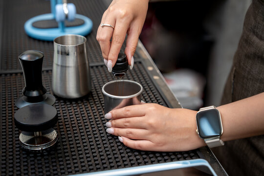 Close up of a barista using coffee distribution needles to break up grounds in a metal dosing cup before espresso brewing.