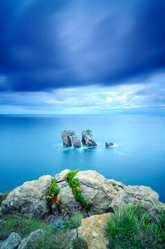 Vertical long exposure of the Urros sea stacks in a blue sea at blue hour, with a mossy rock in front.