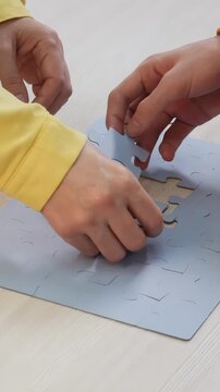 Two hands are working together on a blue puzzle. The hands are placing puzzle pieces onto a flat surface, focusing on the puzzle assembly.