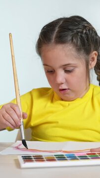 A girl is focused on painting with a brush. She is using watercolors on paper, showcasing her artistic skills and concentration in the creative process.