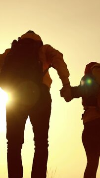 A man and a woman hold hands as they walk together. The sun glows behind them, creating a serene atmosphere during their stroll.