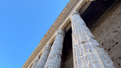 Ancient Roman stone columns and cornice against a blue sky, low angle view, Rome, Italy © dragomirescu
