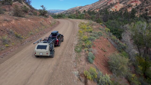 A breathtaking aerial view highlights Hells Backbones rugged beauty, with a teardrop camper and SUV exploring the terrain.