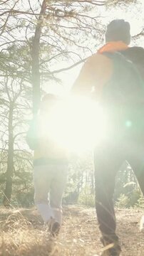 A man and a woman walk through a forest with yellow backpacks. The man wears an orange jacket while the woman wears a blue jacket, enjoying the outdoors.