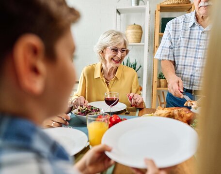 Happy multi-generation family gathering around dining table and having fun during a lunch or dinner on holiday or weekend, senior couple, grandparents, grandmother and grandfather eating