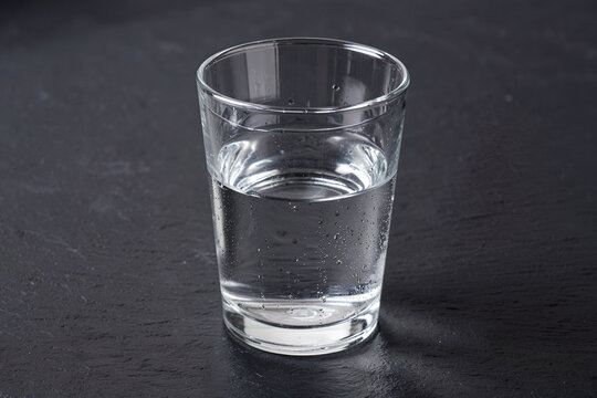 Clear glass tumbler half-filled with water on a charcoal slate surface, low angle