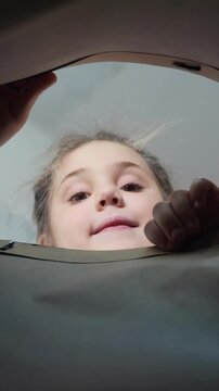 A girl peers curiously into a container, her face framed by the edge. Her hands grip the side as she contemplates what is inside the container.