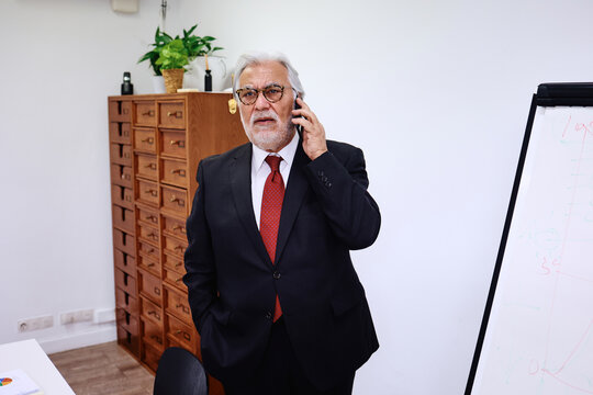Hispanic senior businessman talking by mobile phone and working at office or workplace