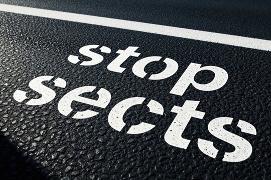 White text stop sects painted on black asphalt road. Warning message about dangerous cults, religious groups. Social issue concept showing prohibition of harmful belief systems. Public awareness