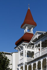 Ornate white wooden balcony and red turret roof of historic resort architecture against blue sky © MarekLuthardt
