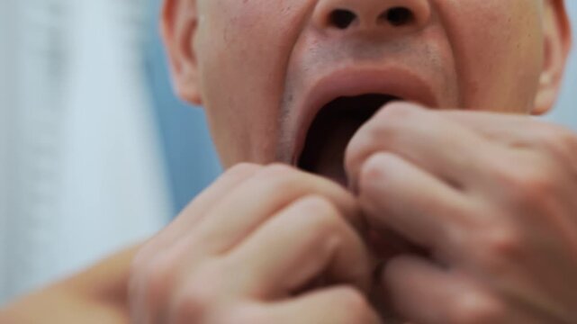Dental flossing and oral hygiene routine performed by an adult man. 4k video closeup of hands cleaning between lower teeth with dental floss to remove plaque and trapped food