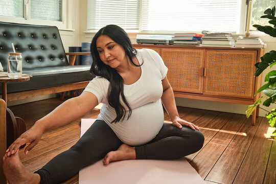 Expecting mother does yoga stretch in sun room at home during pregnancy