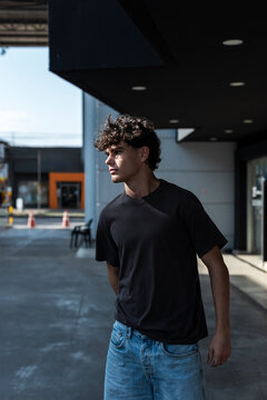 Serious man in a dark t-shirt and jeans looking to the side under a dark canopy in strong light