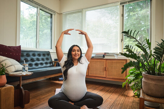 Native American expectant mother stretches in yoga pose in sun room