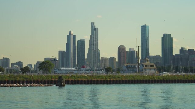 A helicopter flies near the Chicago skyline above the Lake Michigan waterfront on a sunny summer day. Modern skyscrapers and calm water create a dramatic urban cityscape scene.