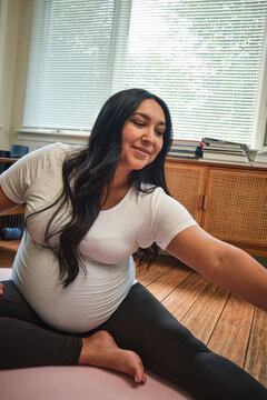 Expecting Native American mother stretches in sun room during yoga