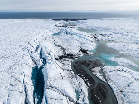 Melting ice cap aerial view with deep glacial crevasses and dark meltwater channels on Arctic ice
