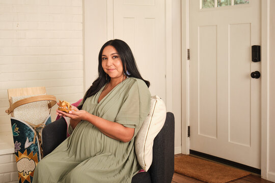 Native American woman seated at home holding a snack during pregnancy
