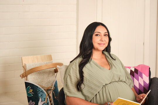 Native American pregnant woman reading a book at home in a cozy setting