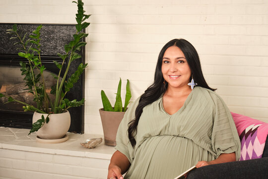 Native American pregnant woman sitting indoors by a fireplace with plants around
