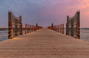 Naklejka premium Symmetrical wooden pier with wrought iron gates at a calm sea during sunset