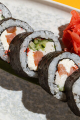 Detailed close-up of traditional Japanese maki sushi rolls wrapped in dark nori seaweed, filled with rice, salmon, cream cheese and fresh vegetables, served with pickled ginger. © vision