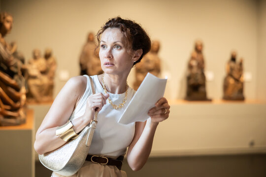 Portrait of middle-aged woman with brochure in her hands examining antique objects in a historical museum