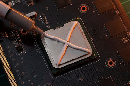 top down view of thermal grease being applied from a tube onto a computer central processing unit on a dark pcb