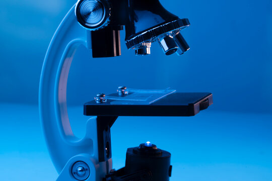 Side view of laboratory microscope analyzing rejuvenating cream sample on glass slide in blue neon light