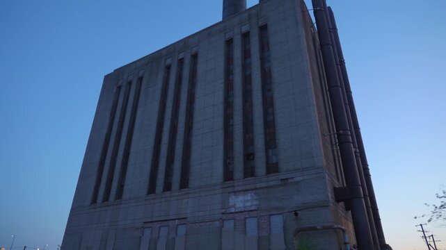 Large industrial power plant building with tall smokestacks under a clear blue evening sky and visible moon. Urban industrial architecture and energy infrastructure create a dramatic city industry