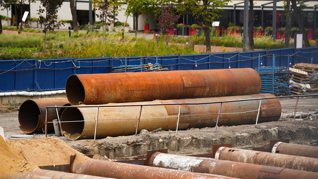Large diameter steel pipes stacked at an active construction site, representing heavy engineering materials, infrastructure development and preparation for foundation or excavation work