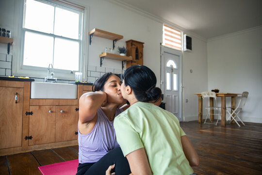Two women kiss during sit-up workout at home