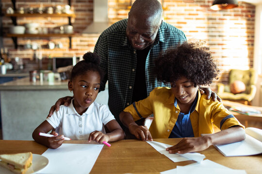 Older man helping kids with paper crafts at kitchen table