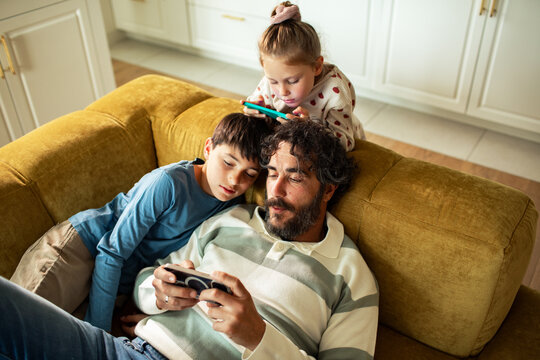 Man with children using smartphones on living room couch