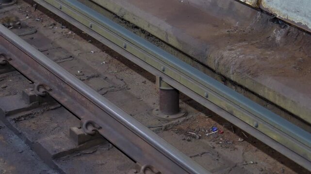 A rat runs beside the train tracks inside a dirty subway or metro station environment. Underground transportation infrastructure, urban wildlife, and gritty public transit conditions create a