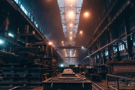Industrial foundry workshop at metallurgical plant filled with heavy machinery, casting equipment and overhead cranes for metal production.