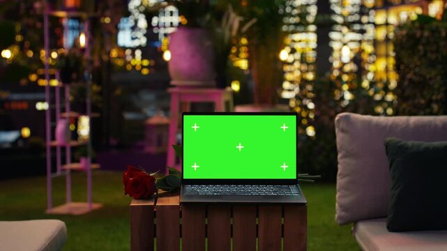 Chroma key notebook and romantic flowers sit on a rooftop restaurant table with city buildings behind, while an isolated-screen laptop rests beside red roses in an elegant outdoor lounge.
