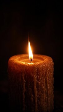 Rustic textured burning candle casting a warm glowing light and flickering flame in the dark creating a spiritual peaceful ambiance
