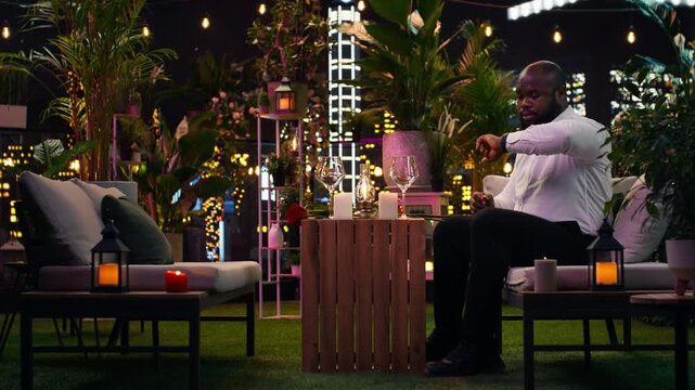 Nervous man waits for his date in an elegant outdoor lounge after arranging flowers, fidgeting anxiously because he worries his girlfriend may be late.