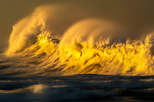 Photograph of a powerful ocean wave breaking over a submerged reef at sunset on the south coast of New South Wales, Australia, captured with a slow shutter speed to create a dreamlike effect.