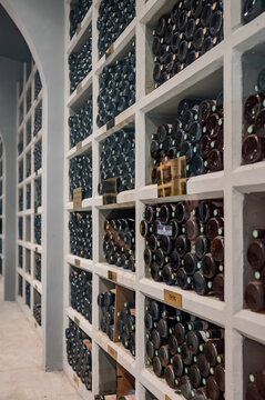 Interior of French wine cellar with rare premium bottles stored by vintage years in organized racks, with bottle labels, corks, stone floor, and warm backlit lighting.