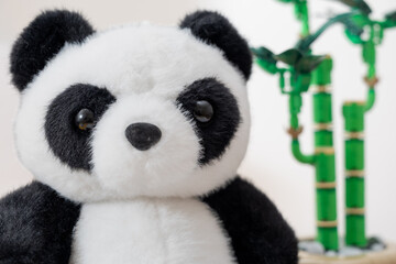 close up of a cuddly plush panda bear with large glossy eyes, looking directly forward against a background of toy block bamboo plants on white © Laurentiu Bratu