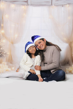Divorced single mother and her 5-year-old Latina daughter with glasses excited celebrate Christmas and New Year's together, wearing Santa hats