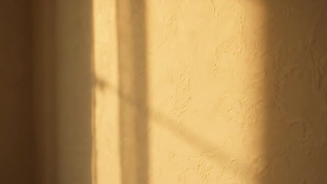 Abstract golden hour sunlight casting window frame shadow on a plain beige wall.