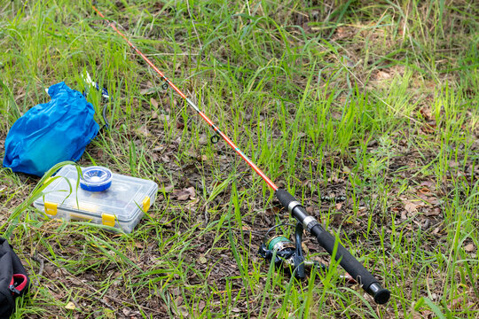 Horizontal wide shot of bright orange fishing rod with tackle gear on grass